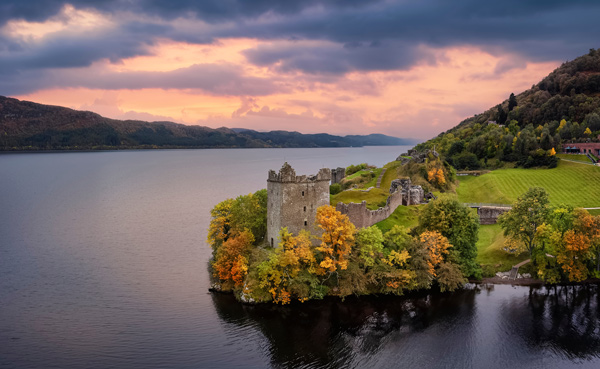 scenic view of a historic castle by a lake surrounded by autumn trees with a colorful sky ideal for photography and travel