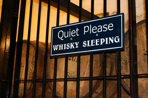 sign that says Quiet Please Whisky Sleeping visible through bars showcasing whisky aging process 6 years old whisky barrels