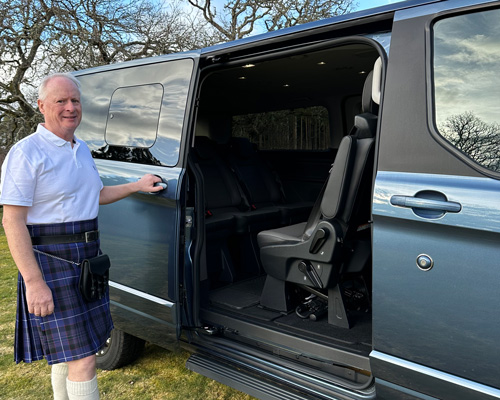 man in a kilt standing beside a van door open showcasing spacious interior with emphasis on six passenger seating options